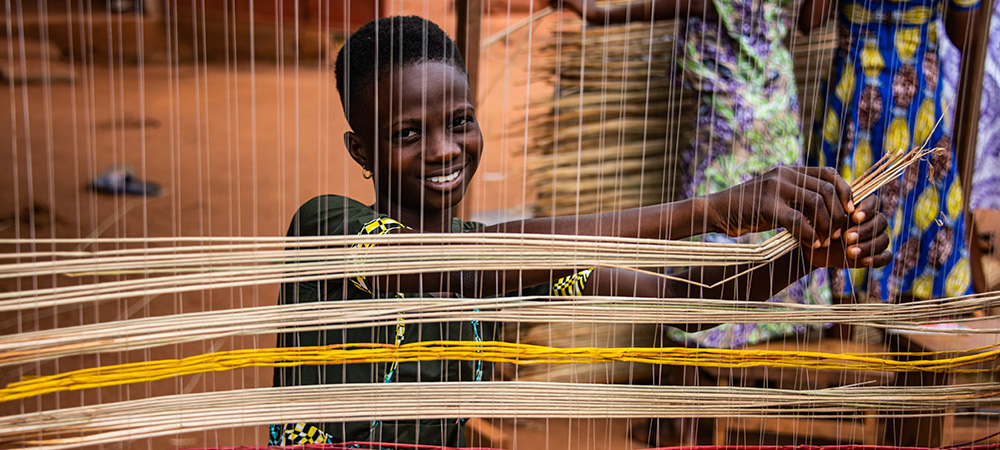 Een meisje uit Togo leert om matten te weven op het project. 