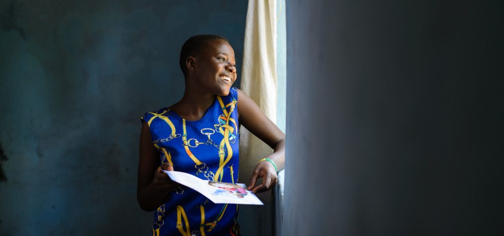 Brenda uit Uganda staat bij een raam en houdt een kerstkaart vast.