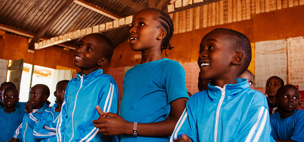 Drie lachende kinderen staan in een klaslokaal in Kenia.
