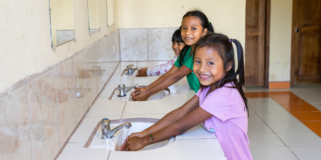 Drie Latijns-Amerikaanse meisjes wassen hun handen bij nieuw gebouwde sanitaire voorzieningen.
