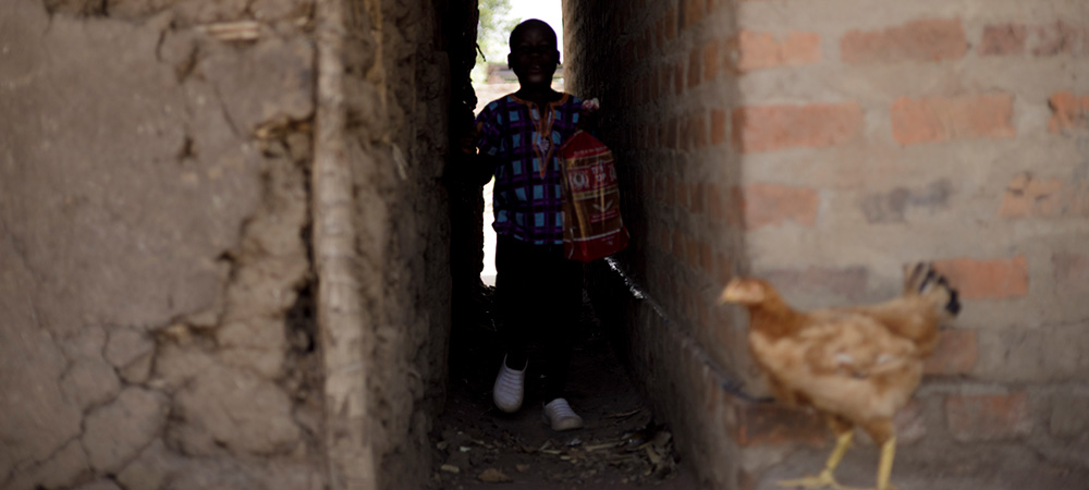 Acaali uit Uganda loopt in een steegje met een zak brood in zijn hand.